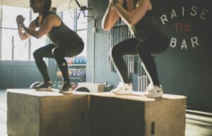 Two people performing box jumps on wooden crates in a gym