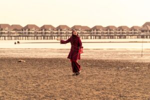 Woman in traditional clothing walking on a sandy beach.