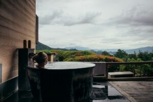 Woman relaxing in an outdoor wooden bathtub with mountain view