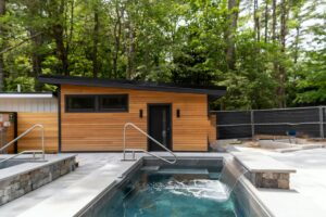 A small wooden cabin beside a stone-lined pool with a waterfall feature